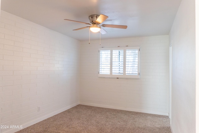 carpeted empty room with ceiling fan and brick wall