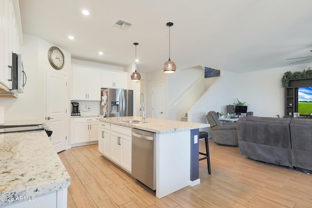 kitchen featuring white cabinetry, stainless steel appliances, decorative light fixtures, and an island with sink