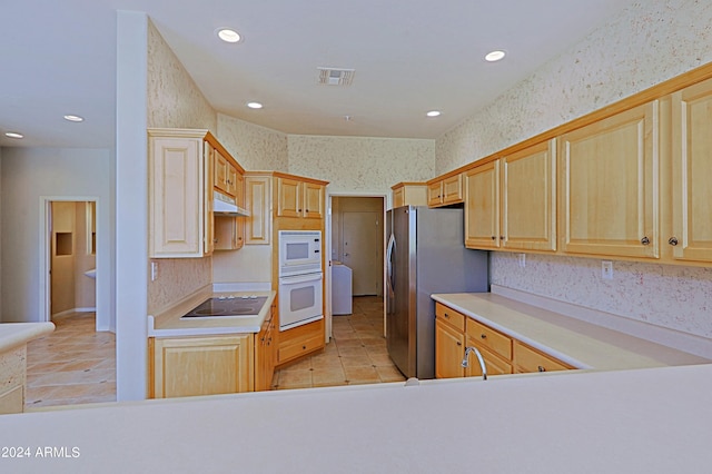 kitchen with electric cooktop, light brown cabinets, stainless steel fridge, and oven