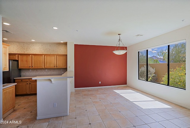 kitchen featuring a breakfast bar, pendant lighting, light tile patterned flooring, decorative backsplash, and stainless steel fridge