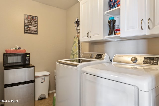 laundry room featuring light tile patterned floors, washing machine and clothes dryer, and cabinets