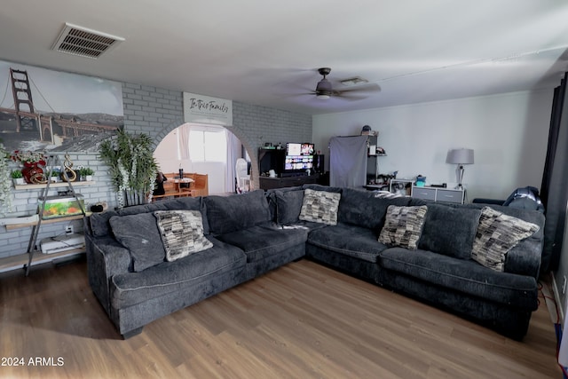 living room with hardwood / wood-style flooring, ceiling fan, and brick wall