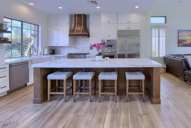 kitchen with appliances with stainless steel finishes, a center island, wall chimney range hood, and a breakfast bar