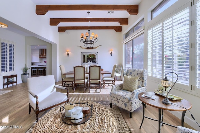 living room featuring a wealth of natural light, a notable chandelier, beam ceiling, and light hardwood / wood-style flooring