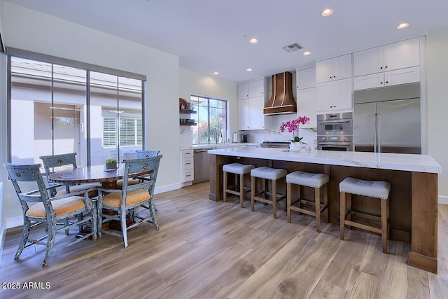 kitchen featuring white cabinets, a center island, wall chimney exhaust hood, and appliances with stainless steel finishes