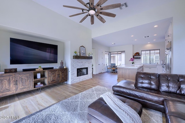 living room with a stone fireplace, light hardwood / wood-style flooring, and ceiling fan