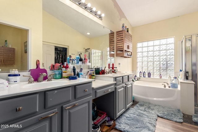 bathroom featuring vanity, wood finished floors, a stall shower, vaulted ceiling, and a garden tub