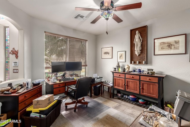 home office with visible vents, a ceiling fan, arched walkways, and a healthy amount of sunlight