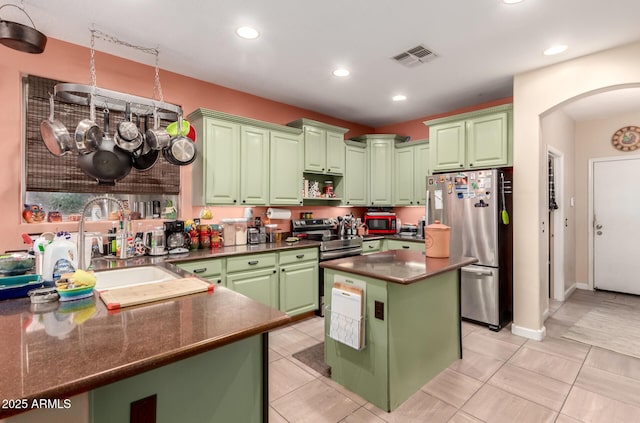 kitchen featuring arched walkways, a sink, appliances with stainless steel finishes, green cabinets, and dark countertops