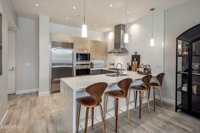 15215 N Kierland Blvd Unit 101, Scottsdale, AZ 85254 - kitchen with built in appliances, wall chimney range hood, a peninsula, light wood-style floors, and light countertops