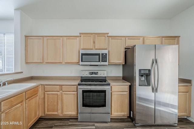 kitchen featuring stainless steel appliances, a sink, light countertops, light brown cabinetry, and dark wood finished floors