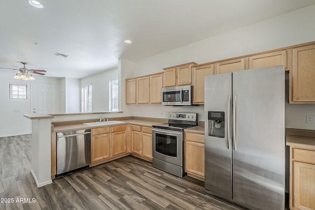 kitchen with light brown cabinets, a peninsula, a sink, appliances with stainless steel finishes, and dark wood finished floors