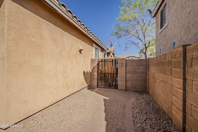 view of side of property featuring a gate, a tile roof, fence, and stucco siding