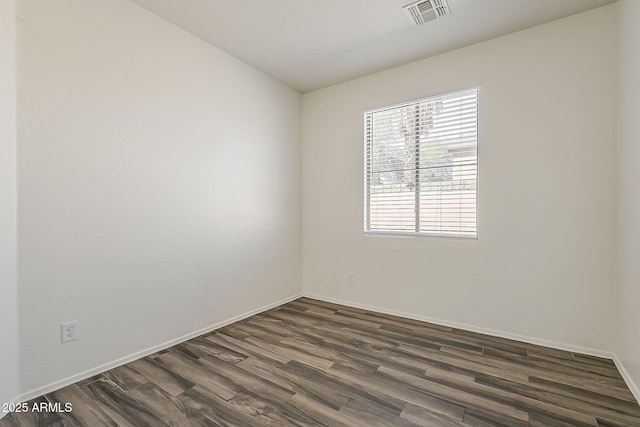 spare room featuring dark wood-type flooring, visible vents, and baseboards