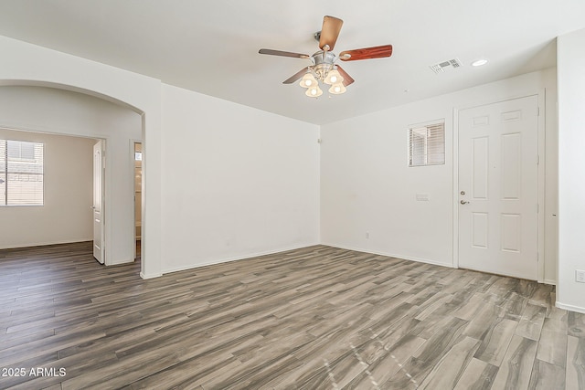 spare room with arched walkways, wood finished floors, visible vents, and a ceiling fan