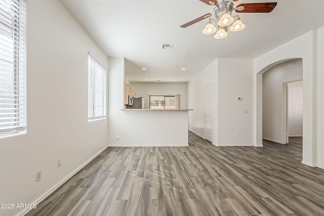 unfurnished living room with arched walkways, visible vents, baseboards, and wood finished floors