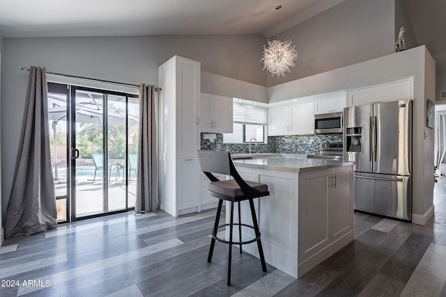 kitchen featuring appliances with stainless steel finishes, tasteful backsplash, white cabinets, a center island, and hanging light fixtures