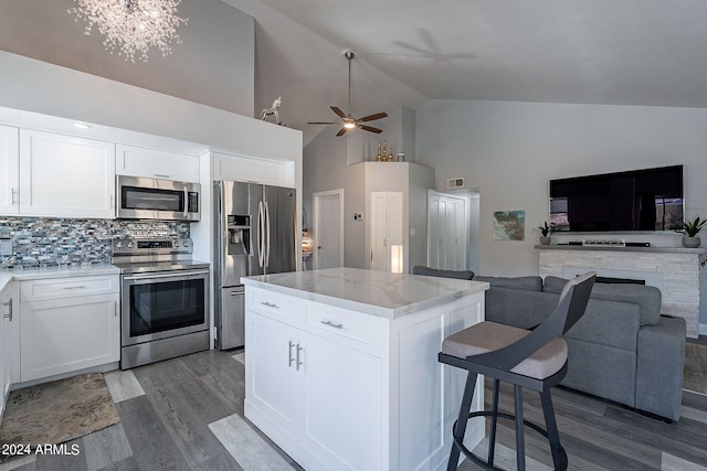 kitchen featuring white cabinetry, a center island, stainless steel appliances, tasteful backsplash, and light stone counters