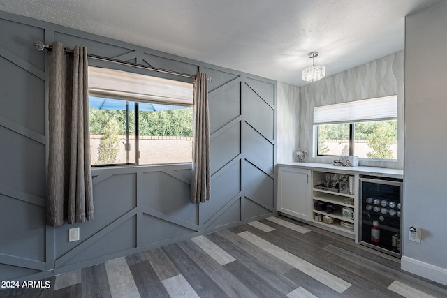 interior space with a chandelier, wine cooler, a wealth of natural light, and dark wood-type flooring