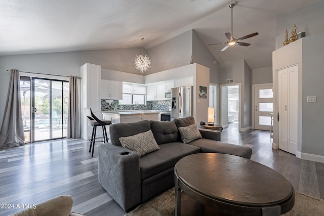 living room featuring sink, high vaulted ceiling, wood-type flooring, and ceiling fan with notable chandelier