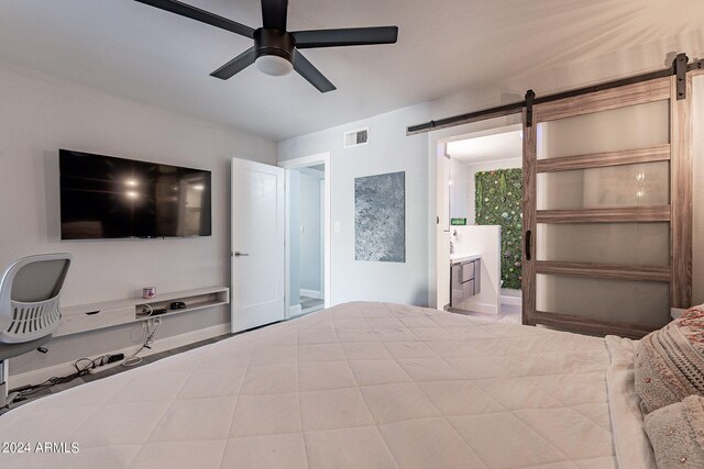 unfurnished bedroom featuring a barn door, ensuite bathroom, and ceiling fan