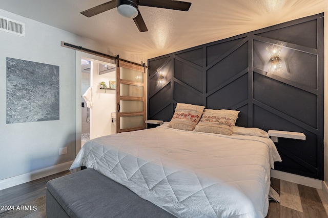 bedroom featuring dark hardwood / wood-style flooring, a barn door, and ceiling fan