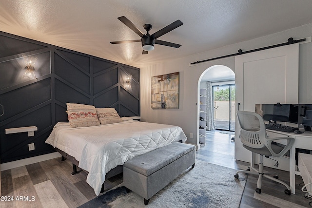 bedroom featuring access to exterior, a textured ceiling, ceiling fan, a barn door, and hardwood / wood-style flooring