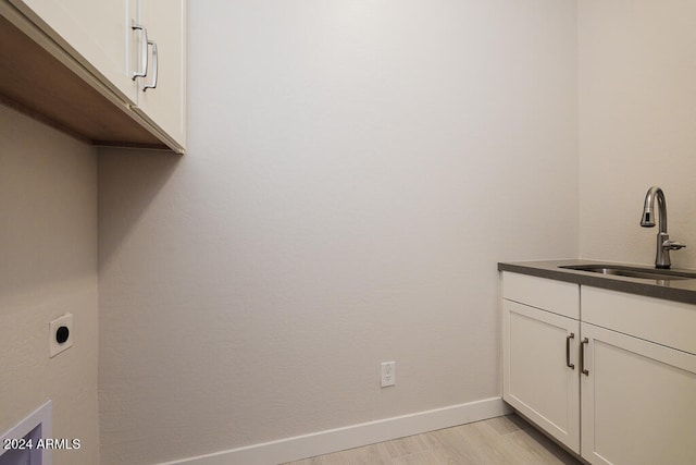 clothes washing area featuring electric dryer hookup, sink, cabinets, and light hardwood / wood-style flooring