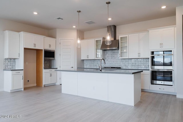 kitchen featuring white cabinets, appliances with stainless steel finishes, a kitchen island with sink, and wall chimney range hood