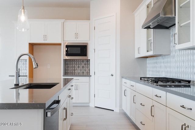 kitchen with pendant lighting, white cabinets, wall chimney range hood, sink, and tasteful backsplash