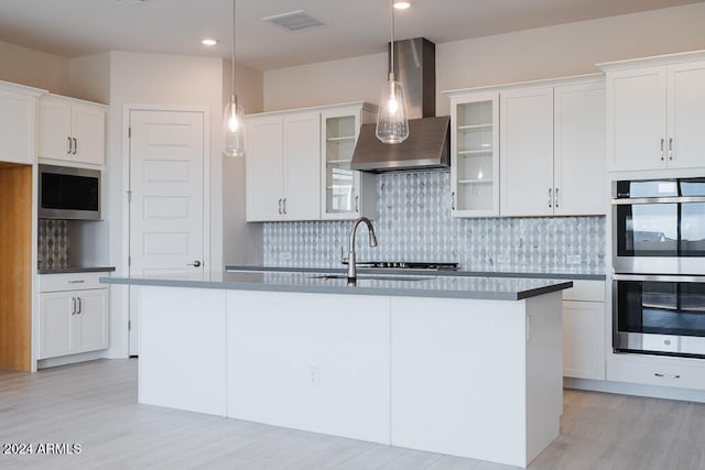 kitchen with pendant lighting, backsplash, white cabinets, wall chimney exhaust hood, and appliances with stainless steel finishes