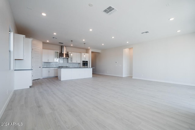 kitchen with decorative backsplash, a kitchen island, wall chimney range hood, pendant lighting, and white cabinetry