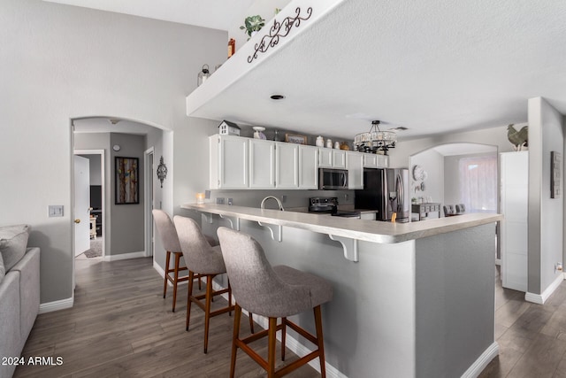 kitchen with kitchen peninsula, appliances with stainless steel finishes, a kitchen bar, dark hardwood / wood-style floors, and white cabinetry