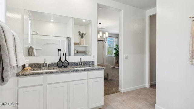 full bath with double vanity, a sink, baseboards, and an inviting chandelier