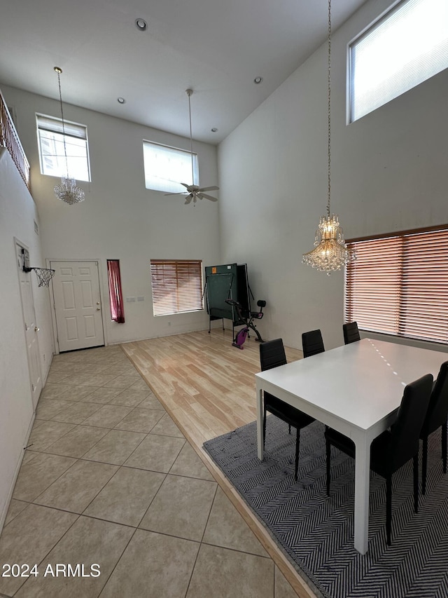 dining space with ceiling fan with notable chandelier, a towering ceiling, and light tile patterned floors