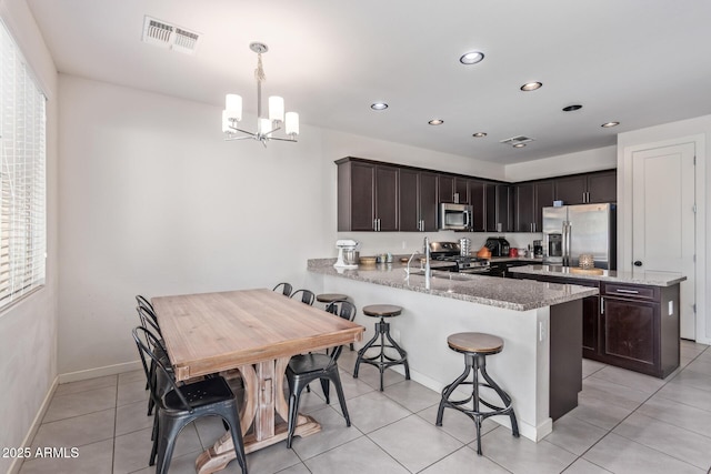 kitchen featuring visible vents, dark brown cabinetry, a kitchen bar, a peninsula, and stainless steel appliances