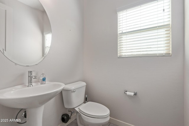 bathroom featuring plenty of natural light, toilet, baseboards, and a sink