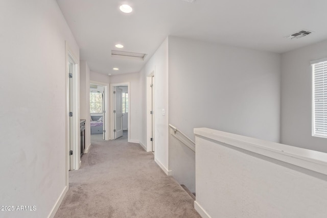 hallway with visible vents, baseboards, attic access, an upstairs landing, and light colored carpet