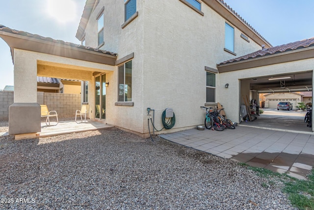 view of property exterior featuring stucco siding, a tile roof, a patio, and fence