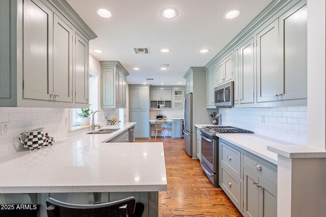 kitchen with visible vents, light wood-style flooring, a sink, stainless steel appliances, and a peninsula