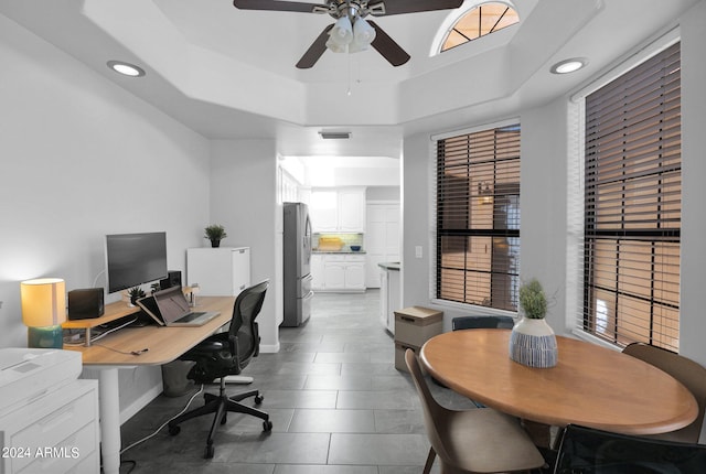 tiled office space featuring a raised ceiling and ceiling fan