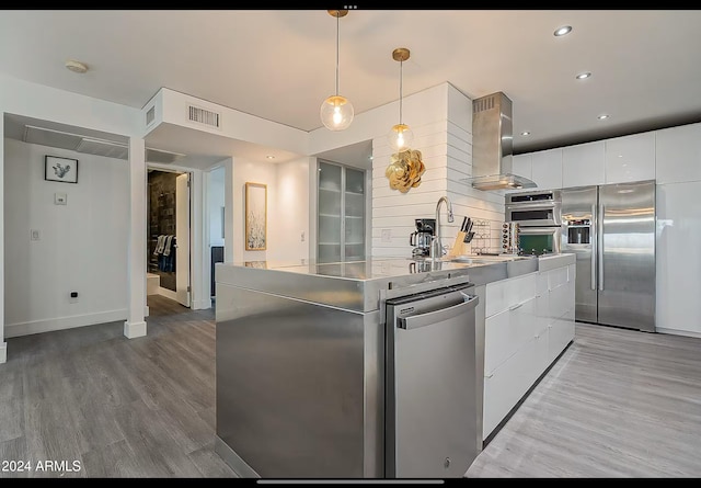 kitchen featuring pendant lighting, wall chimney exhaust hood, light wood-type flooring, appliances with stainless steel finishes, and white cabinetry