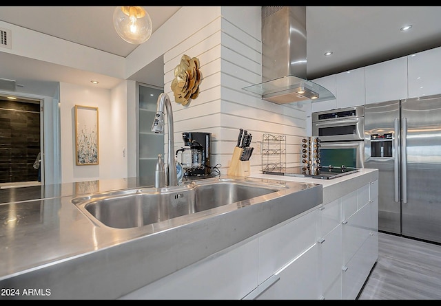 kitchen featuring island exhaust hood, appliances with stainless steel finishes, stainless steel counters, sink, and white cabinetry