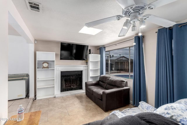 living room with light tile patterned floors, visible vents, a fireplace with raised hearth, ceiling fan, and a textured ceiling