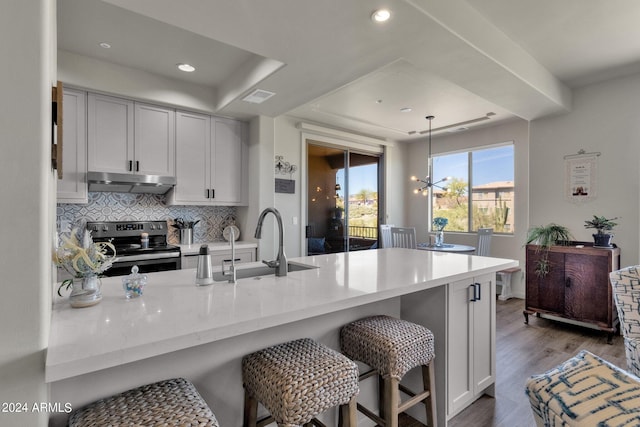 kitchen featuring kitchen peninsula, decorative light fixtures, a breakfast bar area, dark hardwood / wood-style flooring, and stainless steel electric stove