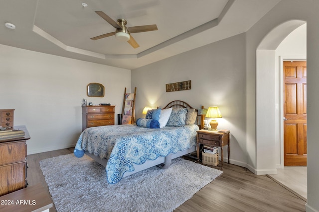 bedroom with wood-type flooring, a raised ceiling, and ceiling fan