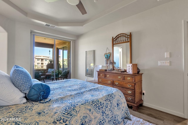 bedroom with access to outside, wood-type flooring, ceiling fan, and a tray ceiling