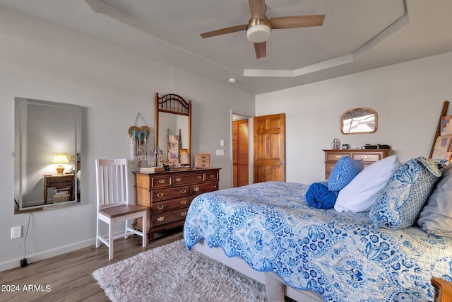 bedroom with a raised ceiling, ceiling fan, and hardwood / wood-style flooring