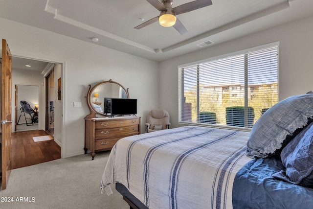 carpeted bedroom with ceiling fan and a raised ceiling