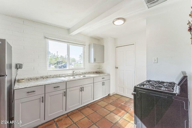 kitchen featuring gray cabinetry, light stone countertops, sink, stainless steel appliances, and beamed ceiling